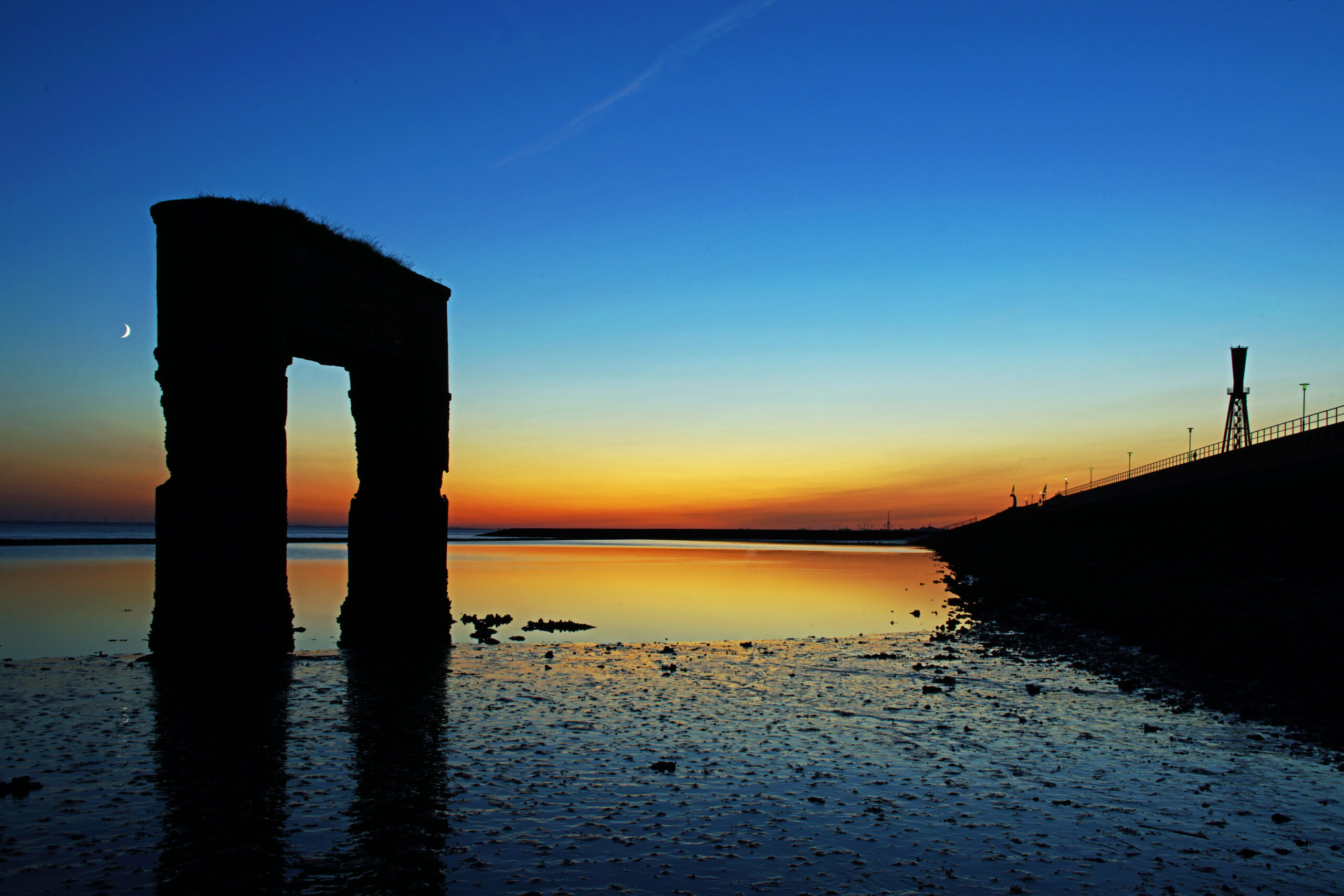 Nordsee Sonnenuntergang am alten Fähranleger in Eckwarderhörne mit dem Leuchtfeuer Preußeneck im Hintergrund blaue Stunde